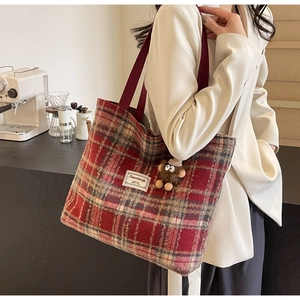 Détail d'un grand cabas à carreaux rouges avec charm peluche sur un blazer blanc