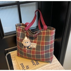 Detail of vintage red plaid canvas tote bag with plush monster charm and brand label