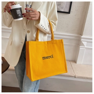 Dettaglio della borsa tote in tela giallo brillante con scritta merci e manici robusti