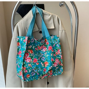 Detail of vibrant green floral tote bag with red roses hanging on a metal rack