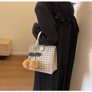 Gros plan d'un sac à lunch en tweed avec poignées en coton et breloque cerise en peluche