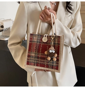 Detail of red plaid linen tote bag with rope handles and brown plush pompom charm