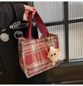 Close-up of red plaid wool tote bag with a plush monster charm and deep red handles