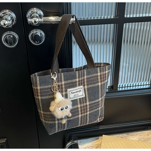 Detail of checkered canvas tote bag with plush charm hanging on a black door handle