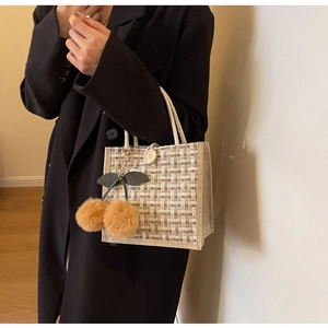 Detail of checkered linen bento bag featuring rope handles and plush cherry charm