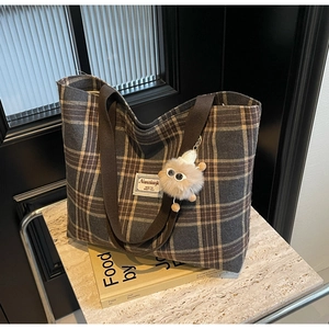 Detail of grey plaid canvas tote bag with brown straps and plush monster charm decoration