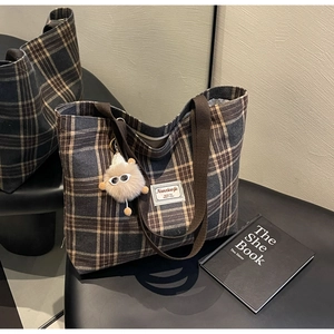 Detail of checkered canvas tote bag with plush eye charm and woven logo tag on a chair