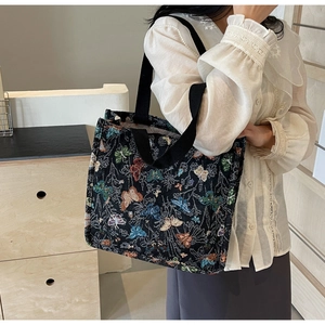 Close-up of a black canvas tote bag featuring colorful jacquard butterfly embroidery detail