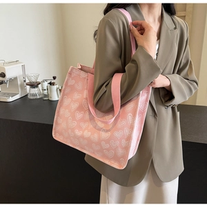 Detailed side view of pink canvas tote bag with white heart patterns worn by a model