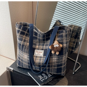 Détail du cabas à carreaux avec anses bleu marine et breloque en peluche sur fond miroir