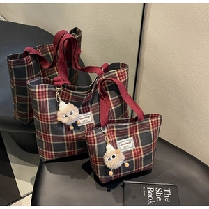 Detail view of red and grey plaid canvas tote bags with plush monster charm accessories