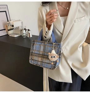 Detail of blue and brown plaid wool tote bag with cute plush monster charm and blue handles