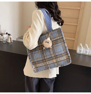 Blue and brown plaid wool tote bag with plush charm shown on person in a modern interior