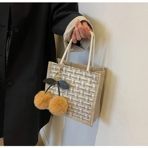 Close-up of beige woven lunch tote featuring a cherry plush charm and sturdy handles