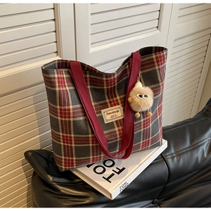 Detail of red and grey checkered canvas tote bag with plush charm on a leather sofa
