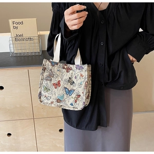 Close-up of a cream canvas tote bag featuring colorful butterfly embroidery and white handles