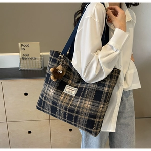 Sac fourre-tout à carreaux avec sangle bleue et breloque singe sur l'épaule du modèle