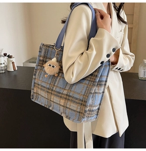 Detail of blue plaid wool tote bag with plush charm on a model in a modern interior setting