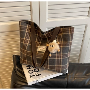 Detail of retro plaid canvas tote with woven strap and plush monster charm on leather