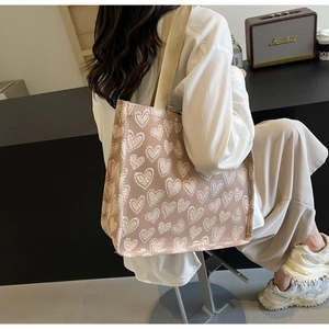Detail view of heart print canvas tote bag with wide strap on shoulder of a model