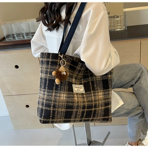 Détail du sac cabas en tartan avec breloque singe en peluche et bandoulière tissée bleue