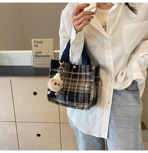 Close-up of tartan wool handbag with dark blue straps and a cute plush monster charm