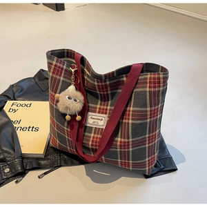 Detail of red plaid canvas tote bag with plush charm on a vintage leather jacket