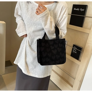 Detail of black canvas tote bag with heart patterns and dual handles in a lifestyle setting