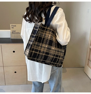Detail of a large tartan wool tote bag with blue straps worn by a model in a modern room
