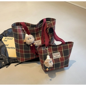 Detail of red and green plaid canvas tote bags with plush charm and woven handles
