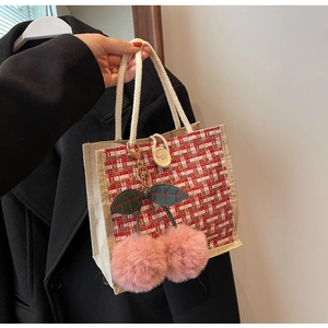 Detail of red checkered woven lunch bag with plush cherry charm and rope handle