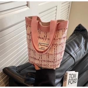 Close-up of pink and beige tweed woven bucket bag featuring brand logo and woven strap