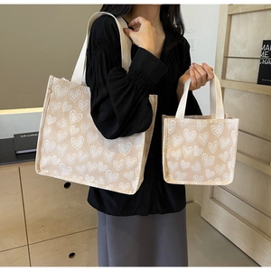 Detail of beige canvas tote bags with white 3D heart pattern in large and small sizes