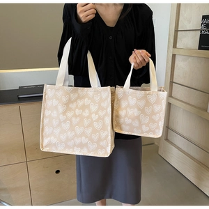 Detail of canvas tote bag set featuring white heart patterns and beige woven handles