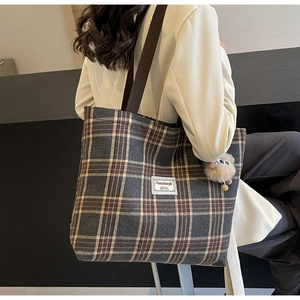 Detail of a large checkered canvas tote bag with brown straps and a plush ball charm