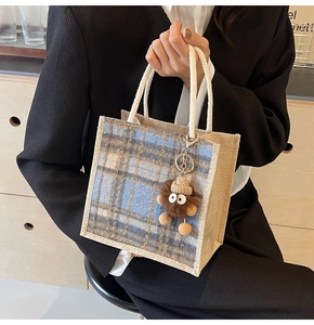 Close-up of linen tote bag featuring a blue plaid pattern and cute plush mascot pendant