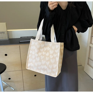 Detail of beige canvas tote bag with white heart embroidery and durable woven handles