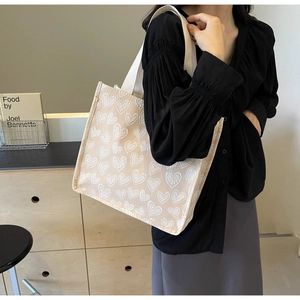 Chic beige canvas tote bag with white heart patterns shown on model in modern room