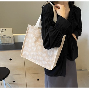 Detail of beige canvas tote bag featuring 3D embossed heart patterns and sturdy handles