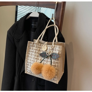 Close-up of beige linen woven lunch bag featuring a plush cherry charm and rope handle