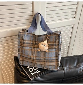 Close-up of wool plaid tote bag with fuzzy monster charm on a fashion book background