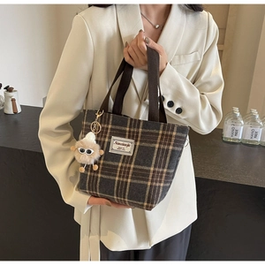 Detail of vintage plaid tote bag with plush charm and branding label on tweed fabric