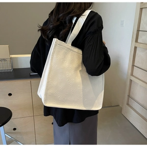 Detailed close-up of white tote bag featuring 3D embossed heart textures and a wide strap