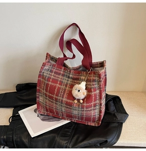 Detail of red plaid fabric tote bag with wine red handle and fun fuzzy doll charm