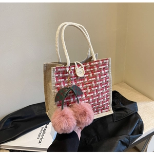 Close-up of woven jute tote bag with tweed paneling and a pink cherry charm detail