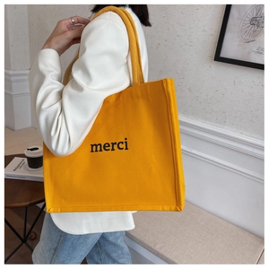 Dettaglio di una borsa tote in tela giallo senape con stampa della scritta merci in nero