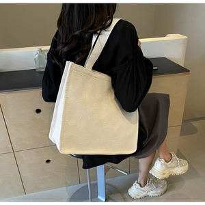Detail of white tote bag with embossed heart pattern shown on model shoulder