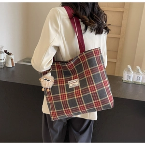 Detailed view of the red plaid canvas tote bag fabric with a plush doll charm