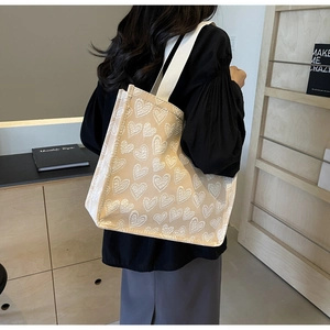 Detail of beige canvas tote bag with white heart embroidery and woven shoulder strap