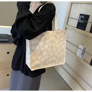Detailed view of beige tote bag with white heart jacquard pattern and sturdy handles